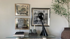 A glass-top table with books, a sculpture, and a black lamp. - Unique Design | Hot Tub | Brookside | Gathering Pl (Tulsa)