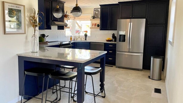 A modern kitchen with dark cabinetry, a central island with bar stools, stainless steel appliances, and pendant lighting. - Unique Design | Hot Tub | Brookside | Gathering Pl (Tulsa)