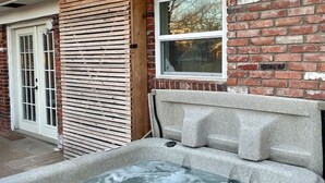 A hot tub with a wooden slatted enclosure and a brick wall in the background. - Unique Design | Hot Tub | Brookside | Gathering Pl (Tulsa)