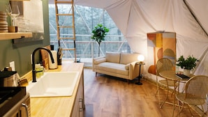 A cozy interior with a wooden floor, a white sofa, a dining table with chairs, a large window, and a kitchen area with a sink and utensils. - "The Perch" RRG - Modern Elevated Stay w/ Hot Tub (Campton)