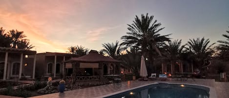 A pool area with a tiled deck, palm trees, and a building with arched windows.