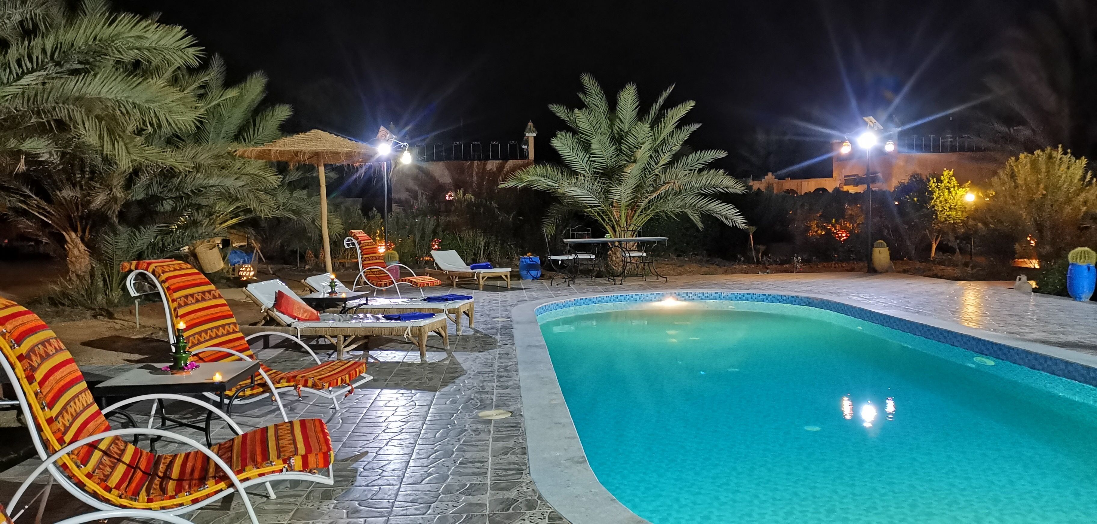 Area piscina illuminata di notte con poltrone a sdraio e vasca.