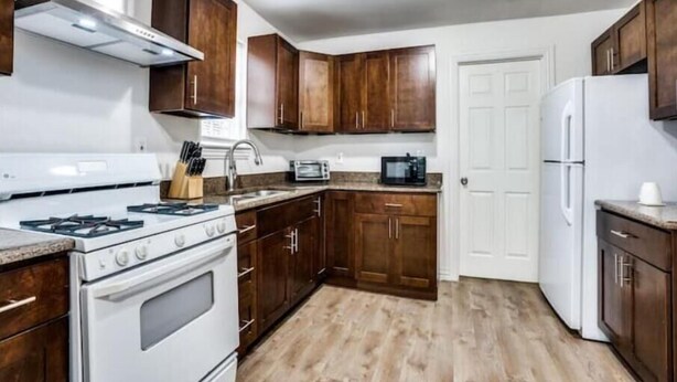 A kitchen with wooden cabinets, a white stove, a microwave, and a refrigerator. - Cozy House (Dallas)