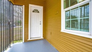 A covered porch with a white door and a window with blinds. - Cozy House (Dallas)
