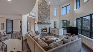 Una sala de estar moderna con chimenea de piedra, un sofá modular grande, una mesa de centro de madera y un televisor.