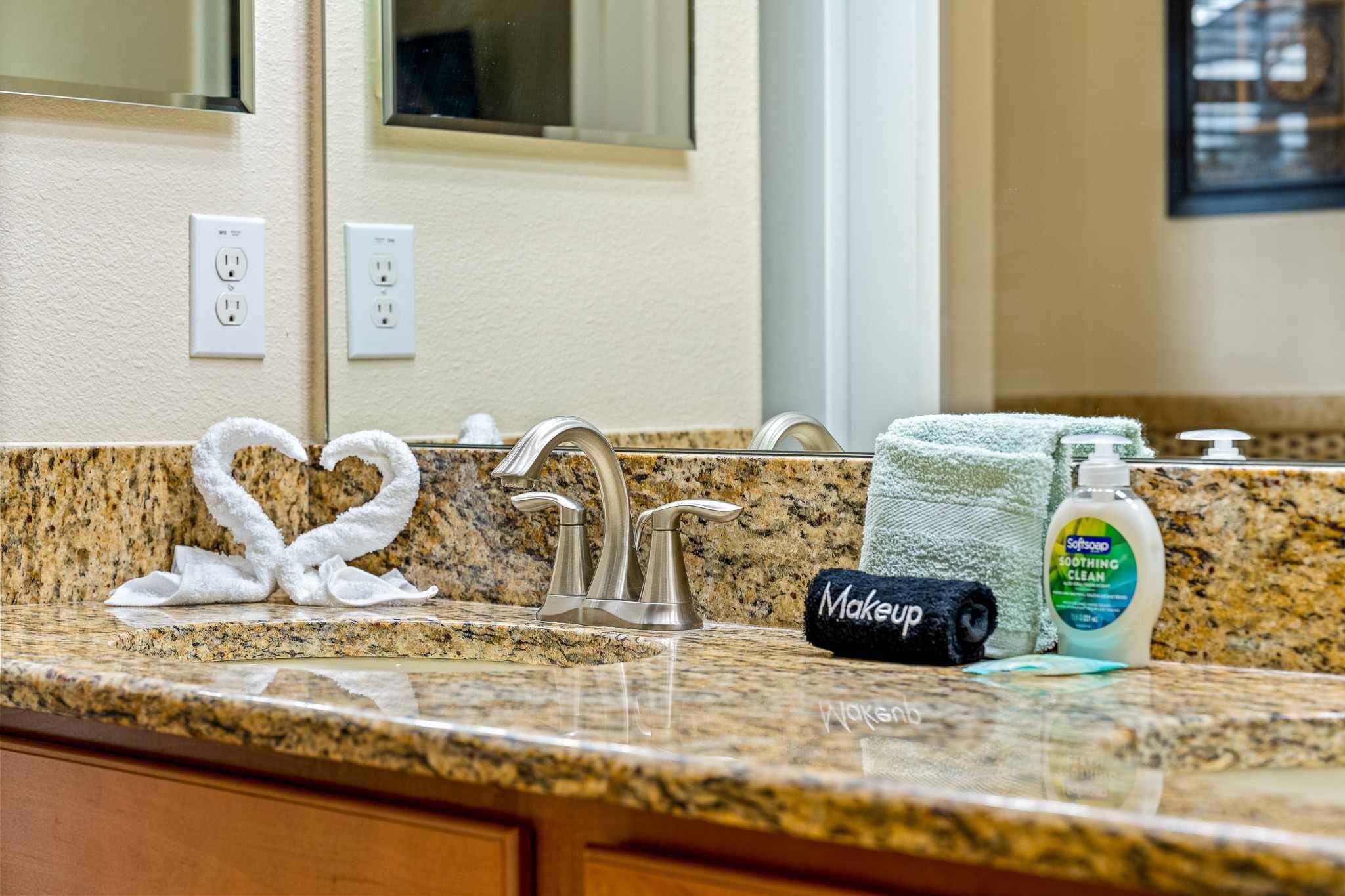 A bathroom with a granite countertop, two faucets, a soap dispenser, and a towel rack with a folded towel.