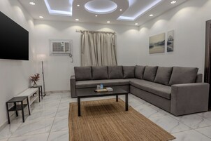 A modern living room with a sectional sofa, a coffee table, a flat-screen TV, a small side table, and a ceiling light fixture.