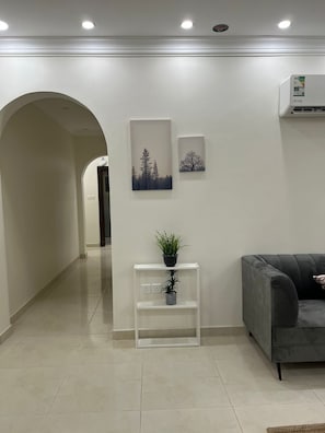 Een moderne woonkamer met een grijze bank, een witte console tafel met planten, en twee ingelijste foto’s aan de muur.