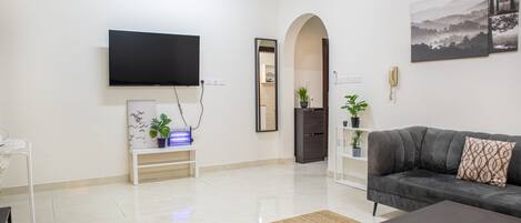 A modern living room with a flat-screen TV, a sofa, a coffee table, and a mirror.