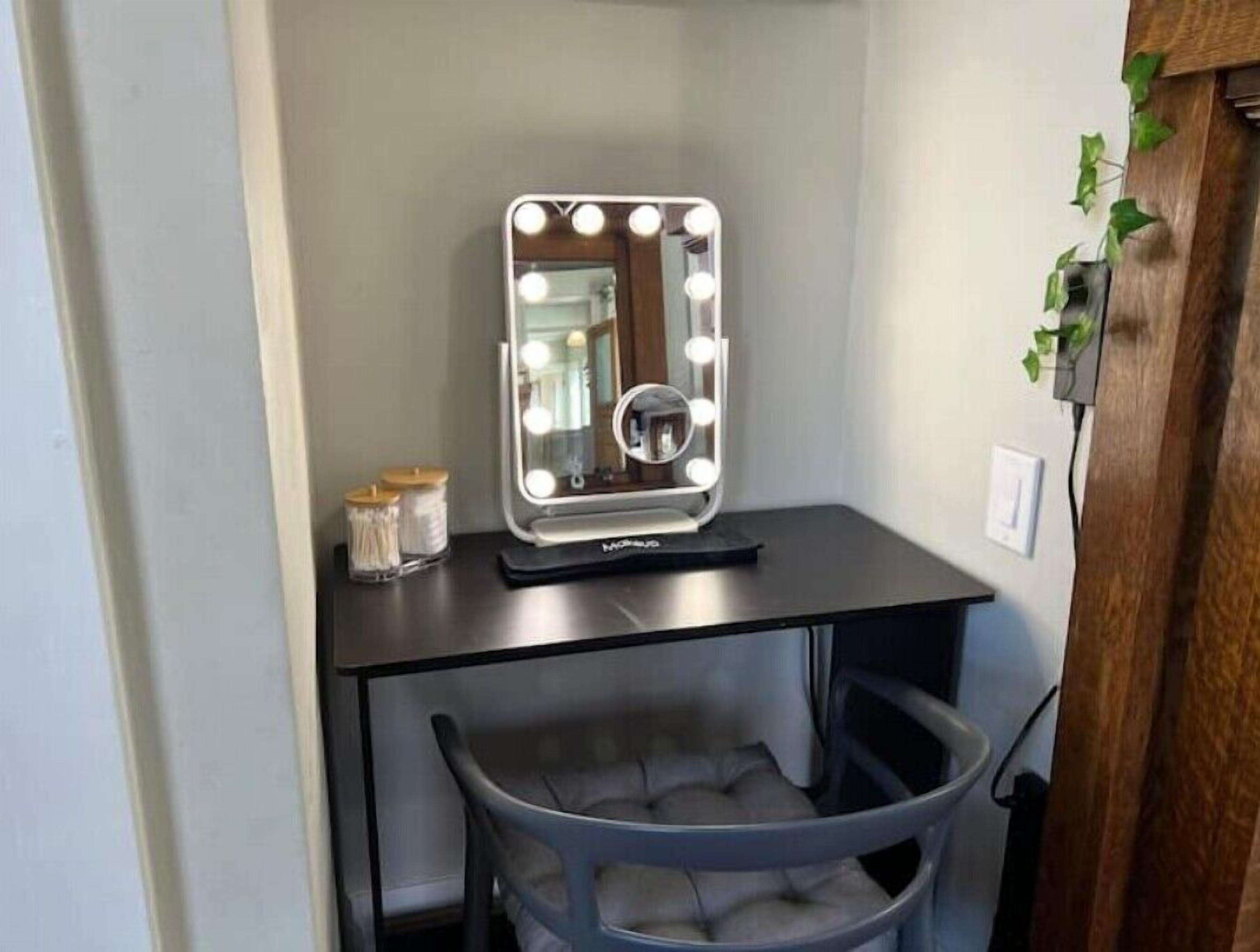 A vanity with a mirror, lights, and a chair.