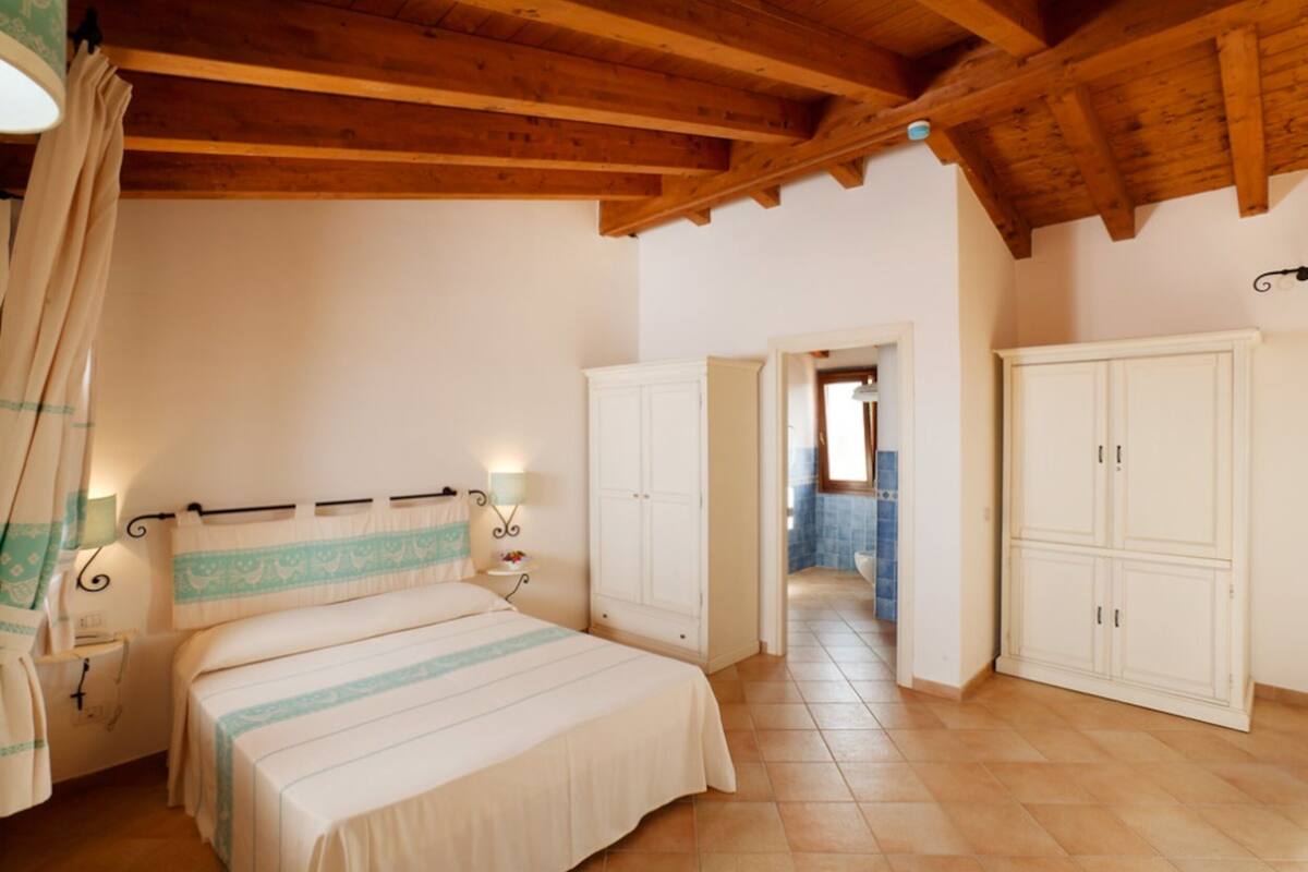 A bedroom with a bed, nightstands, a wardrobe, and a bathroom visible through an open door.