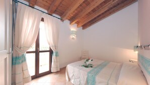 A bedroom with a bed, a window with curtains, a wall-mounted light, and a wooden ceiling.