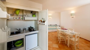 A compact kitchen with a sink, stove, and shelves, and a dining area with a table and chairs. - Residence with pool in Vignola Mare  (Aglientu)