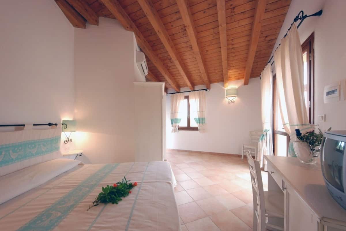 A bedroom with a wooden ceiling, a bed with a floral arrangement, a bedside table, and a television.
