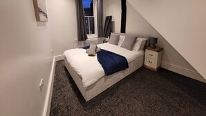 Ein Schlafzimmer mit Bett, Nachttisch und einem Fenster mit Vorhängen.