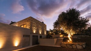 A modern house with a stone facade, a large tree, and a well-lit entrance. - Triades Villas 3, Traumhafte Natursteinvilla mit Salzwasserpool, Ruhige Umgebung (Sivas)