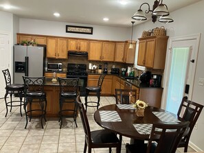 A kitchen with wooden cabinets, a refrigerator, a stove, and a dining area with a table and chairs. - Cheerful 6BR between LSU & NOLA (Baton Rouge)