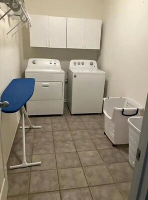 A laundry room with two washing machines, a blue chair, and a laundry basket. - Cheerful 6BR between LSU & NOLA (Baton Rouge)