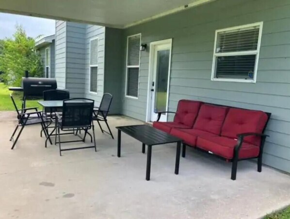 A covered patio with a red sofa, a table, and chairs. - Cheerful 6BR between LSU & NOLA (Baton Rouge)