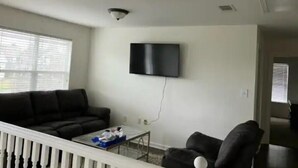 Un salón con un sofá negro, una mesa de centro y un televisor montado en la pared.
