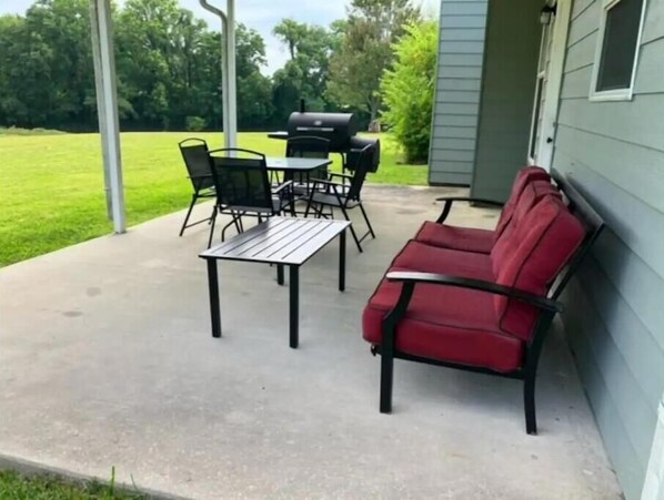 An outdoor patio with a red sofa, a metal table, and black chairs.