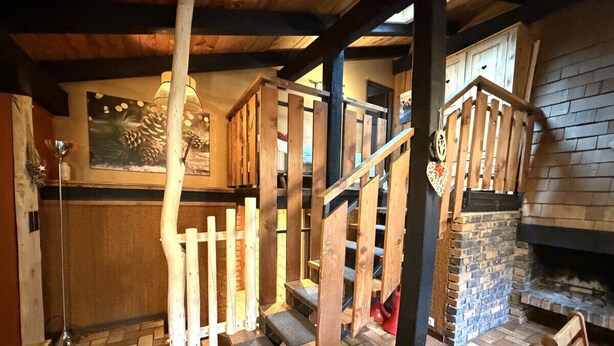 Un escalier en bois au design rustique, une cheminée en pierre et un parquet à motifs en chevrons.