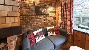 Une pièce chaleureuse avec un mur en briques, un canapé gris agrémenté de coussins à motifs d’ours, un tableau représentant un ours et des rideaux à motifs.