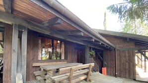 Un bâtiment rustique en bois, doté d’un porche couvert, de bancs en bois et d’un escalier menant à un niveau supérieur.