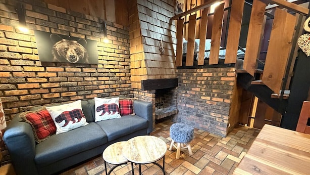 Un salon chaleureux avec une cheminée en briques, un canapé agrémenté de coussins à motifs d’ours et une petite table ronde.