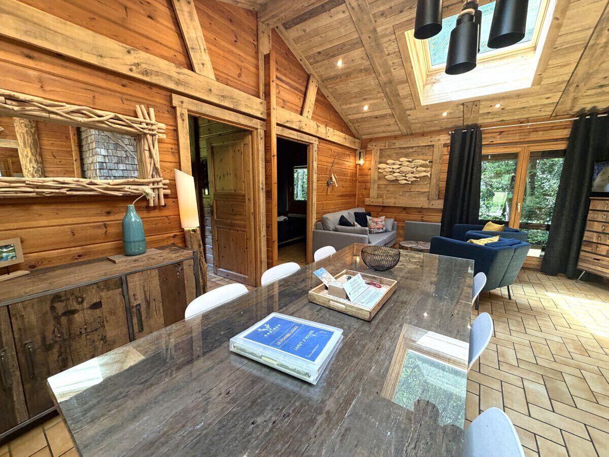 A wooden cabin interior with a dining table, chairs, a sofa, and a fireplace.