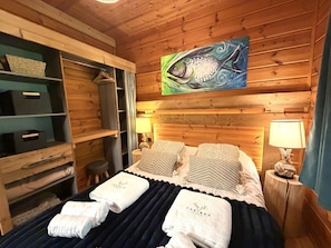 Ein holzgetäfelter Raum im Blockhausstil mit einem Bett, Handtüchern, einem Gemälde und einem Regal mit Körben.
