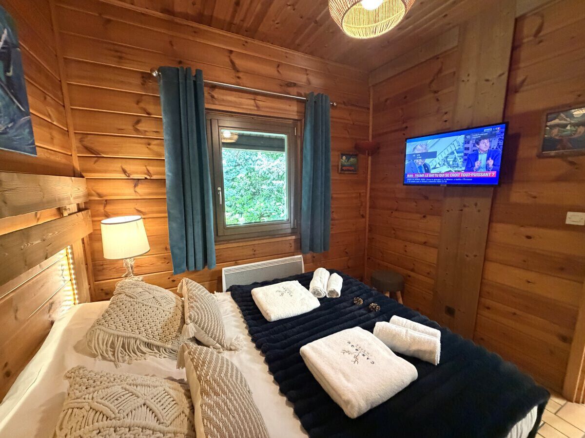 A wooden cabin room with a bed, a TV, and a window with curtains.
