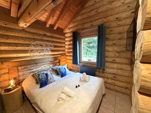 Une chambre dans un chalet en rondins, avec un lit, des oreillers, une fenêtre et un plafond en bois.