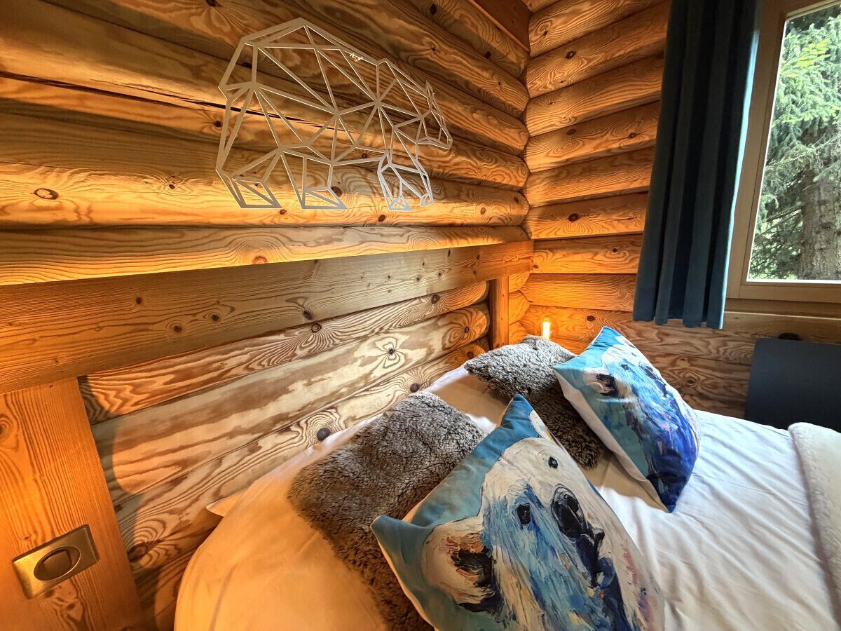 A wooden cabin interior with a bed, pillows, and a geometric light fixture.