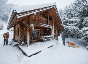 A log cabin with a porch, a snow-covered roof, and a snowman.