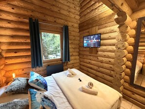 A log cabin room with a bed, a TV, and a window with curtains. - L'OURS BLANC Chalet en rondins (La Bresse)