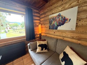 A log cabin interior with a sofa, bear-themed pillows, a lamp, and a bear painting on the wall.