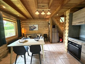 A wooden interior with a dining table, chairs, a refrigerator, and a kitchen area. - L'OURS NOIR Chalet en rondins (La Bresse)
