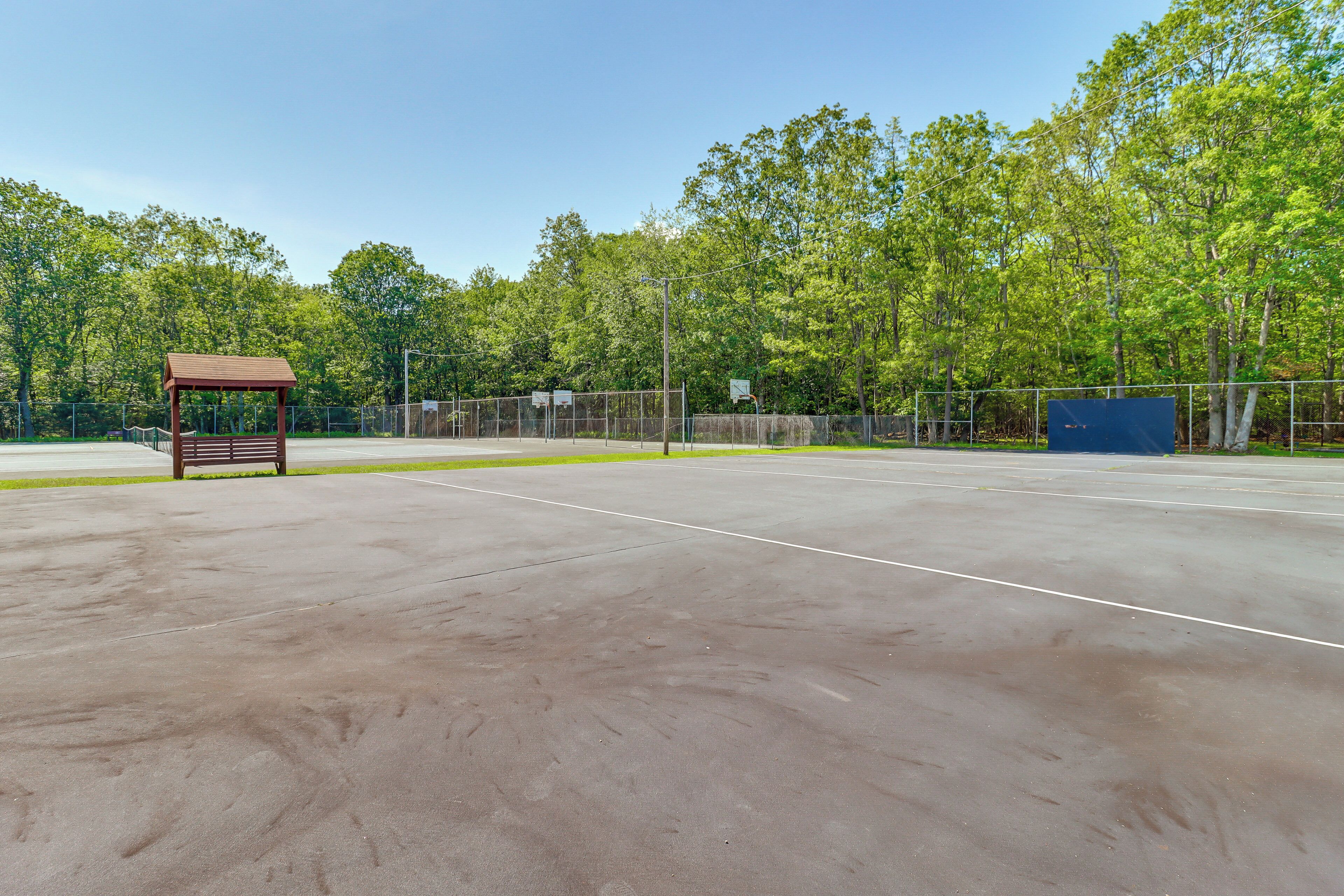 Una cancha de tenis al aire libre con un banco de madera y una estructura azul al fondo.