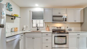 Una cocina moderna con armarios blancos, electrodomésticos de acero inoxidable y una ventana con persianas.