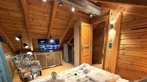 A cozy wooden cabin room with a bed, a television, a colorful chair, and a wooden door. - LE RENNE  Chalet en bois au calme avec SPA Jacuzzi (La Bresse)