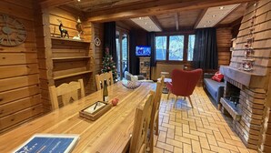 A cozy wooden cabin interior with a dining table, chairs, a fireplace, and a television in the background. - LE RENNE  Chalet en bois au calme avec SPA Jacuzzi (La Bresse)