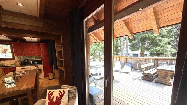 A wooden interior with a dining area, a sofa with a decorative pillow, and a sliding glass door leading to an outdoor deck. - LE RENNE  Chalet en bois au calme avec SPA Jacuzzi (La Bresse)