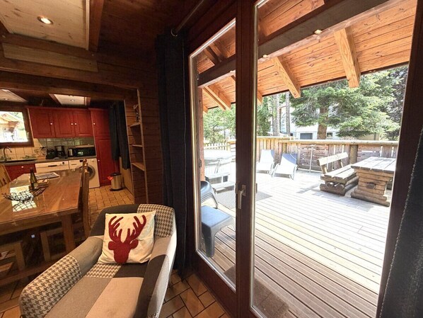 A wooden interior with a dining area, a sofa with a decorative pillow, and a sliding glass door leading to an outdoor deck.