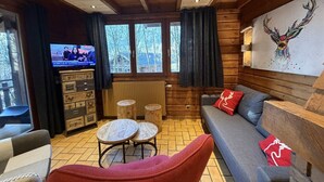 A cozy cabin interior with a wooden ceiling, a sofa, a red chair, a television, and a large window. - LE RENNE  Chalet en bois au calme avec SPA Jacuzzi (La Bresse)