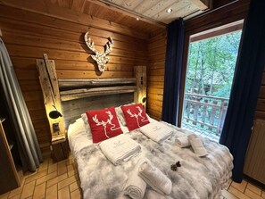 A wooden cabin-style room with a bed, a mounted deer head, and a window with a view of trees.