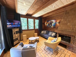 Interior acolhedor de uma cabana com lareira, paredes de madeira, um sofá e uma televisão.
