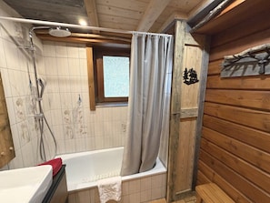 Puisesta mökistä löytyvä kylpyhuone, jossa on kylpyamme, suihku ja pieni ikkuna.