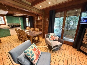 Een knus interieur van een chalet met een eethoek, een bank met kussens, een televisie en uitzicht op de natuur.