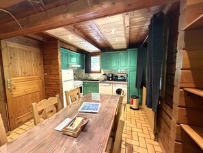 A wooden interior with a dining table, chairs, a kitchen area with green cabinets, and a wooden door.